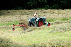 Historischer Traktor Eicher Diesel, luftgekühlt - Baujahr ca. 1950; der Traktor zieht einen alten Heuwender auf einer Wiese am Rand des Rantzauer Forst in Barmstedt, Kreis Pinneberg - Schleswig Holstein.