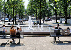 Sprudelnder Brunnen - Zentrum von Ahrensburg, Kreis Stormarn. Familien sitzen in der Sonne auf Bänken am Brunnenbecken.