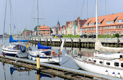Segelboote im Sportboothafen Glückstadt an der Unterelbe - die Schiffe liegen am Steg im Binnenhafen. Auf der anderen Seite des Hafenbeckens historische Häuser der Stadt.