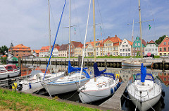 Segelboote im Sportboothafen Glückstadt an der Unterelbe - die Schiffe liegen am Steg im Binnenhafen. Auf der anderen Seite des Hafenbeckens historische Häuser der Stadt.