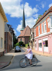 Heiligen Geist Kirche in Barmstedt, Kreis Pinneberg - Radfahrerin in Fahrt; blauer Himmel weisse Wolken.