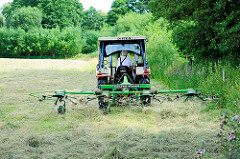 Heuernte auf einer Wiese in Bünningstedt / Ammersbek - ein Landwirt wendet mit seinem Traktor und dem Heuwender das gemähte Gras.