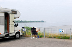 Stellplätze für Wohnmobile am Hafen Glücksstadt - eine Besucherin der Stadt sitzt neben ihrem Wagen im Campingstuhl und liest die Zeitung - im Hintergrund die Einfahrt zur Unterelbe.