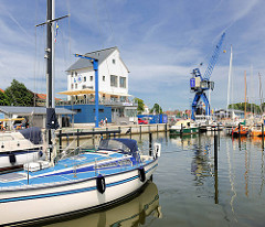 Hafenspeicher und Kran - Sportboothafen in der Stadt Schleswig. Segelboote liegen am Steg; blauer Himmel mit Schleierwolken.