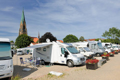 Weisse Wohnmobile stehen am Hafen der Stadt Schleswig - im Hintergrund der Turm vom St. Petri Dom.