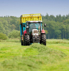 Heuernte in der Gemeinde Tangstedt / Kreis Stormarn. Ein Traktor mit Hänger nimmt das getrocknete Gras auf.