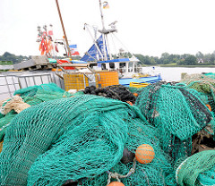 Stapel grüne Netze am Kai vom Fischereihafen in Kappeln - im Hintergrund die Schlei und ein Fischereischiff.