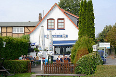 Fährhaus, Restaurant und Cafe an der Fähre über die Schlei bei Arnis. Gäste sitzen in der Sonne im Garten.