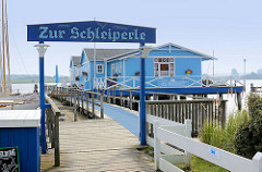 Holzhaus, blau gestrichen an der Schlei in Arnis - Zur Schleiperle, Restaurant und Cafe auf dem Wasser.