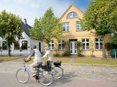 Lange Strasse in Arnis, der kleinsten Stadt Deutschland - historische Fischerhäuser; Fahrradfahrer auf ihren Rädern in Fahrt.