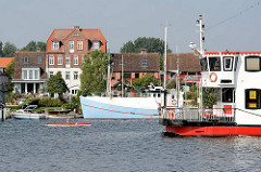 Schiffsverkehr auf der Schlei  - Fahrgastschiff und Kanu auf dem Wasser; am Ufer ein Fischereiboot - Häuser der Stadt Arnis.