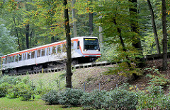 Bahnstrecke Walddörferbahn - endgültig eröffnet 1921; ein U-Bahnzug fährt auf einer Trasse zwischen Bäumen Richtung Station Großhansdorf.