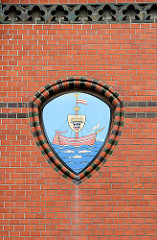 Wappen der Hansestadt Wismar an der Ziegelfassade / Backsteinfassade des historischen Postgebäudes. Schwimmende Kogge, schwarzer Stierkopf - Möwe, drei Fische.