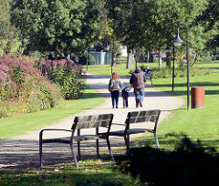 Kurpark Mölln - 2007 unter Denkmalschutz gestellt - 1968 eröffnet, Entwurf Hamburger Gartenarchitekt Gustav Lüttge. Holzbänke am Weg - SpaziergängerInnen in der Sonne.