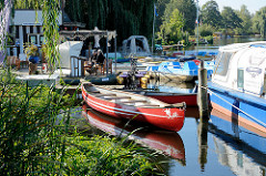 Bootsvermietung  am Stadtsee von Mölln - ein rotes Kanu liegt am Schilf des Sees - im Hintergrund Tretboote.