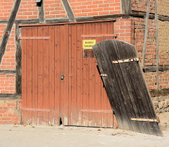 Garagentor an einem Fachwerkhaus in Mölln; in den Angeln hängende schiefe Holztür.