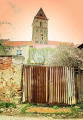 Wellblechtor an einer Mauer mit abbröckelndem Putz - im Hintergrund der Kirchturm der gotischen Marienkirche in Anklam, Mecklenburg-Vorpommern.