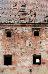 Ziegeldach mit Löchern - Dachpfannen liegen lose auf dem Dach - Ziegelmauer mit Fensterlöchern - Ruine in Mehlsack / Pieniężno, Polen.