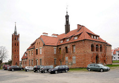Altes Rathaus von  Mehlsack / Pieniężno, Polen. Das Backsteingebäude steht leer - das Dach wurde neu gedeckt - lks. der von Karl Friedrich Schinkel entworfene Kirchturm der ehem. evangelischen Kirche.
