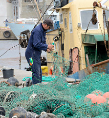 Fischereihafen an der Ostsee in Łeba, Polen - ein Fischer repariert ein Netz.