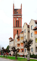 Kirchturm der neogotischen Architektur der katholischen Kirche in Mehlsack / Pieniężno, Polen. Mehrstöckige Wohnhäuser, Neubauten am Marktplatz der Stadt.