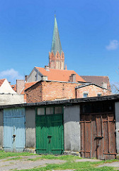 Garagen mit farbigen Holztüren - hinter den Hausdächern der Kirchturm der Marienkirche in Trzebiatow / Treptow an der Rega.