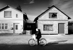 Wohnhäuser - Einzelhaus, unterschiedliche Fassadengestaltung / Klinkerfassade, Ziegelfassade + glatt verputzte Hausfassade - Radfahrer in Fahrt, Schwarz-Weiss Darstellung.