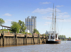 Ein Schiff liegt an der Kaimauer im Hafen von Itzehoe - im Hintergrund Industriearchitektur, Silogebäude.