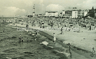 Historisches Motiv Strandleben in Warnemünde - im Hintergrund Häuser und Leuchtturm - Touristen am Strand, Strandkörbe.