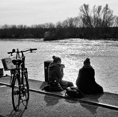 Picknick im Hafen von Itzehoe - zwei Frauen sitzen auf der Kaimauer an der Stör und essen ein Sandwich / Gegenlichtaufnahme, schwarz-weiss.