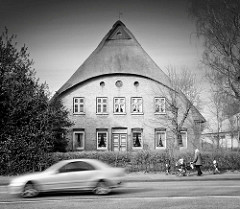 Wohnhaus mit Reetdach an der Hauptverkehrsstrasse Westerstrasse in Elmshorn - schnell fahrendes Auto, Mutter mit Kinderkarre und Kindern.
