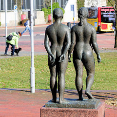 Bronzefiguren, zwei nackte Frauen, Rückansicht - im Hintergrund Bushaltestelle auf dem Theodor Heuss Platz in Itzehoe.