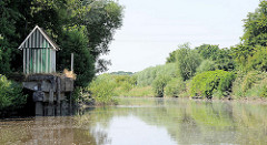Alte Kaianlage aus Beton an der Krückau / Hafen von Elmshorn; dicht bewachsenes Flussufer.