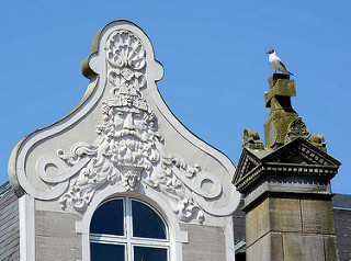 Aufwändiges Fassadendekor - Gründerzeitgebäude am Marktplatz in Eutin - eine Möwe sitzt auf der Spitze der Stele des Gefallenendenkmals.