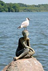 Bronzeskulptur DIE SCHAUENDE am Grossen Eutiner See; Bildhauer Karl Heinz Goedtke - eine Möwe sitzt auf dem Kopf der Figur am Seeufer.