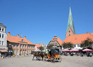 Marktplatz der Kreisstadt Eutin; links das Witwenpalais - re. die St. Michaeliskirche; Anfang des 13. Jahrhunderts als dreischiffige Basilika erbaut. Eine Pferdekutsche fährt über den Platz - Restaurant Tische unter Sonnenschirmen