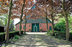 Kopfsteinpflaster, Ahornbäume mit jungen Blättern - historisches Bauernhaus in Neuendorf b. Elmshorn.