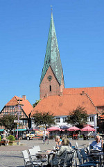 Tische eines Cafés und Restaurants in der Sonne auf dem Marktplatz von Eutin - Kirchturm der St. Michaeliskirche; Anfang des 13. Jahrhunderts asl dreischiffige Basilika erbaut.