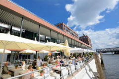 Neubauten in der Hamburger Hafencity - Elbarkaden am Magdeburger Hafen / Aussengastronomie mit Sonnenschirmen am Wasser.
