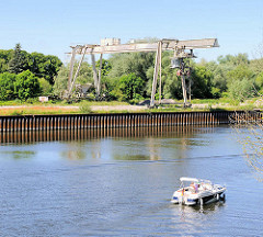 Alter Hafenkran am Ufer der Havel in Havelberg - ein Sportboot fährt flussabwärt Richtung Elbe.