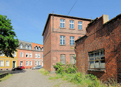 Altes leerstehendes Fabrikgebäude, Ziegelarchitektur - im Hintergrund einstöckige Wohnblocks im ausgebautem Dachgeschoss und farbigen Fassaden.
