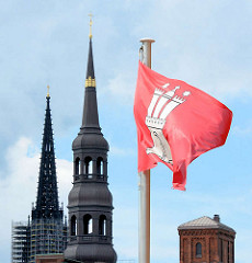 Hamburg Flagge im Wind - rote Fahne mit weissem Wappen; Kirchtürme St. Katharinen und St. Nikolai mit Baugerüst.