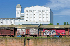 Eisenbahnwaggons mit Graffiti - Industriearchitektur, weisse Fassade; Gewerbegebiet am Handelshafen.