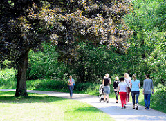 Spazierweg unter Bäumen am Ufer der Wandse in Hamburg Wandsbek - Spaziergängerinnen in der Sonne.