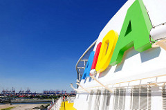 Schornstein der AIDAluna mit buntem AIDA Schriftzug - im Hintergrund Containerkräne im Hamburger Hafen.