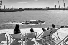 Blick von der Terrasse am Unileverhaus in der Hamburger Hafencity auf die Norderelbe; am gegenüber liegenden Elbufer Hafenkräne im Hafenstadtteil Kleiner Grasbrook. Ein Fahrgastschiff der Hafenrundfahrt Maritime Circle Line fährt Richtung Landungsbrü
