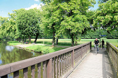 Holzbrücke über die Stepenitz, Fahrradfahrer - im Hintergrund die Hagenpromenade, Bäume - Grünanlage.