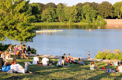 Stadtparksee in der Abendsonne - ParkbesucherInnen liegen auf der Wiese am Seeufer - Boote auf dem See; Bilder aus Hamburg Winterhude.