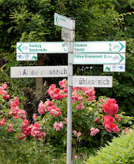 Hinweisschilder für Fahrradtouren - Ortschilder in Seestermühe; blühende Rosen am Strassenrand.
