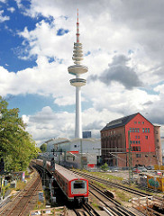 Blick über die Gleise an der Station Hamburg Sternschanze - ein Zug fährt ein; im Hintergrund der Hamburger Fernsehturm, Heinrich Hertz Turm.